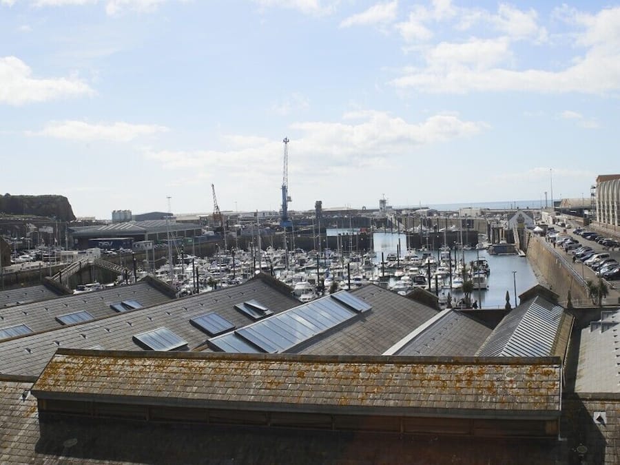 Un puerto deportivo con barcos, un faro y edificios industriales.