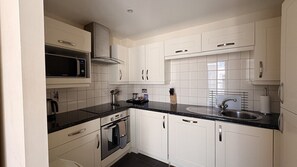 A kitchen with white cabinets, a black countertop, a microwave, an oven, a sink, and a stove. - Liberty Wharf Apartments (St. Helier)