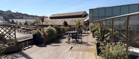 A rooftop patio with wooden decking, outdoor seating, and potted plants.