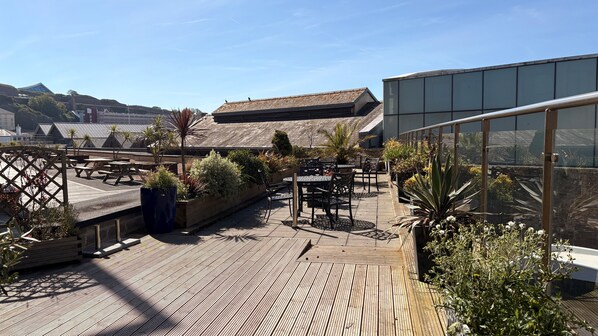 A rooftop patio with wooden decking, outdoor seating, and potted plants. - Liberty Wharf Apartments (St. Helier)