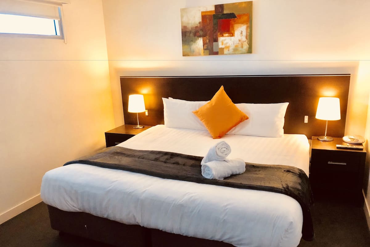 Un lit bien fait, avec du linge de lit blanc, deux tables de chevet avec des lampes et un tableau au mur.