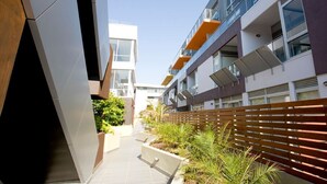 A modern apartment building with balconies, a wooden fence, and a pathway with planters. - St Kilda Central Apartment Hotel (St Kilda)