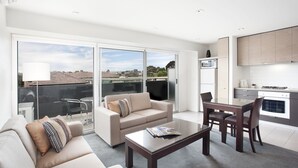 A modern living room with a sofa, coffee table, and dining area. - St Kilda Central Apartment Hotel (St Kilda)