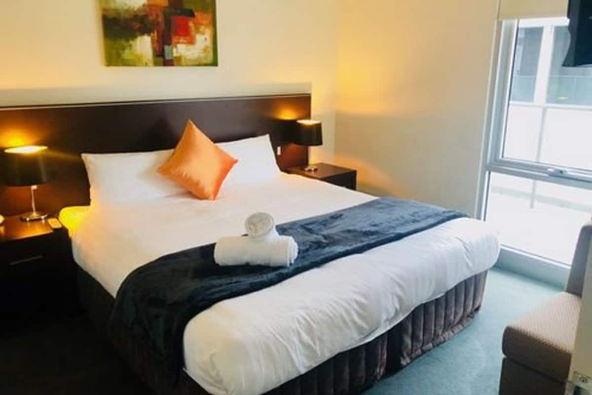 Une chambre d’hôtel avec un grand lit, deux lampes de chevet, une fenêtre et un tableau au mur.