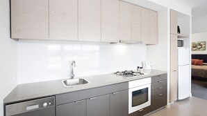 A modern kitchen with grey cabinets, a stainless steel sink, and a built-in oven. - St Kilda Central Apartment Hotel (St Kilda)