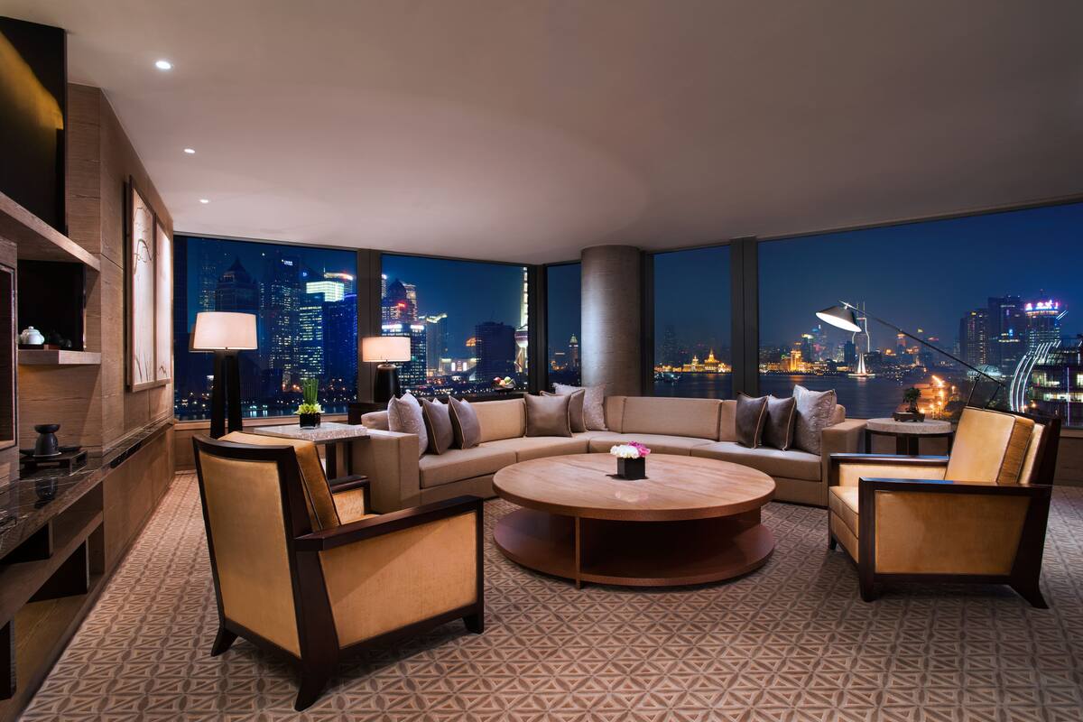 A modern living room with a large sofa, armchairs, a coffee table, and a city view.
