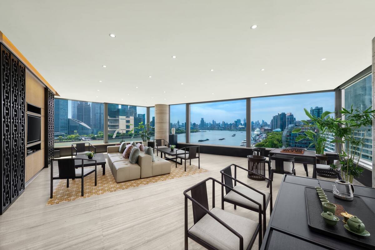 A spacious living area with a large window offering a city view, a sofa set, and a dining table with chairs.