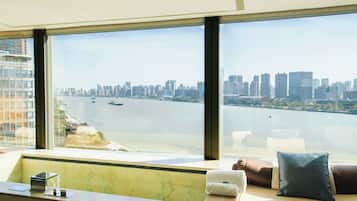 A high-rise hotel room with a large window overlooking a city skyline and a body of water.