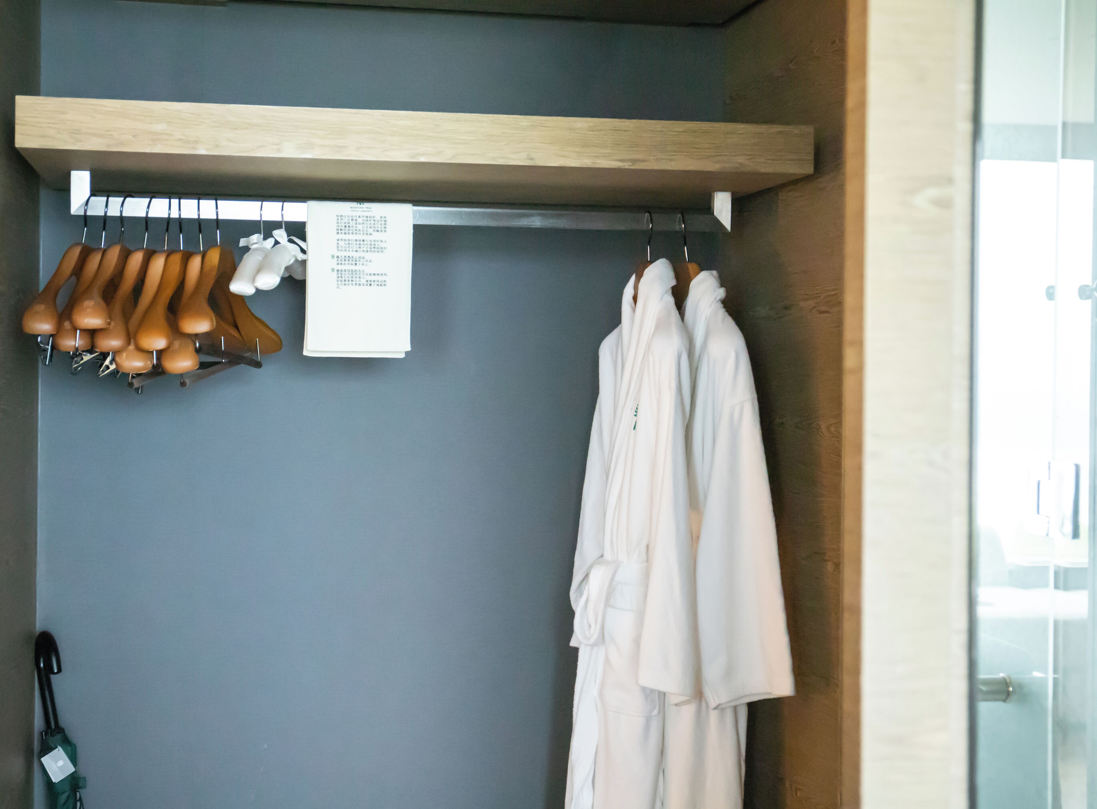 Una habitación con un estante de madera, un zapatero y una bata colgada en la pared.