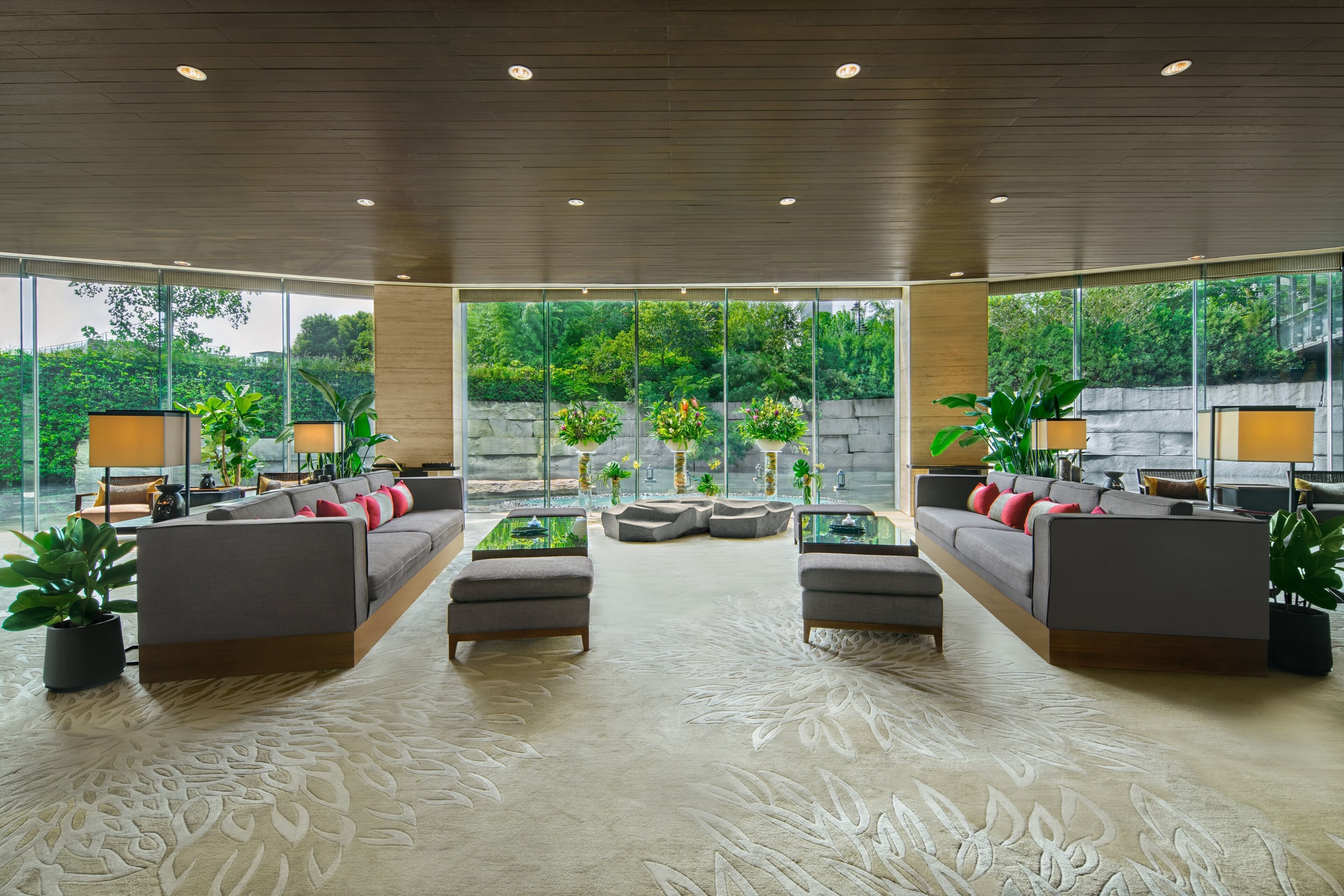 A spacious living area with a modern design, featuring a large sofa set, a coffee table, and potted plants.