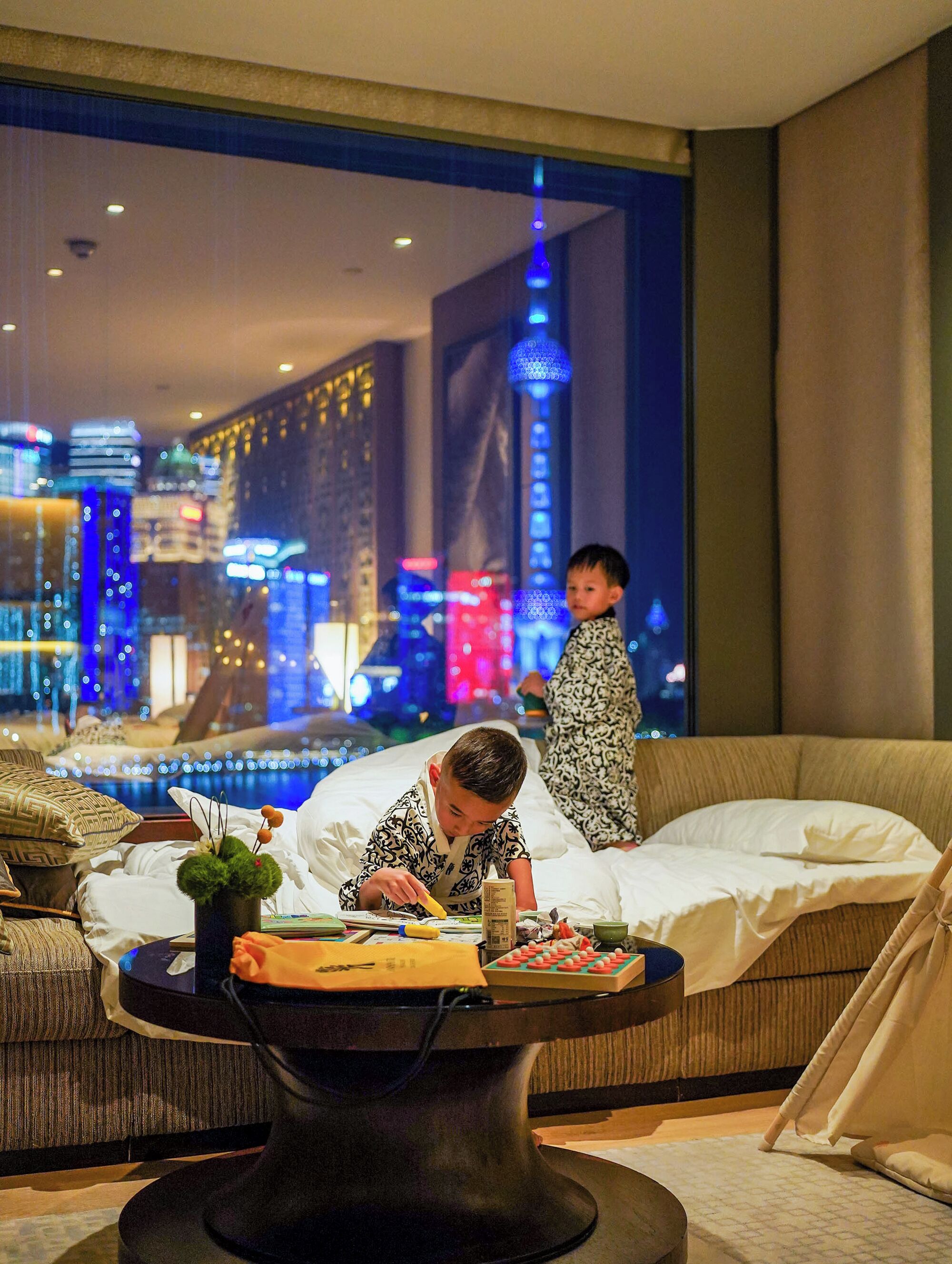 A child playing with toys on a bed in a hotel room with a view of a cityscape.