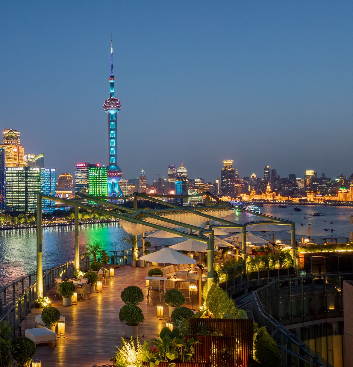 A waterfront restaurant with outdoor seating overlooking a city skyline at dusk.