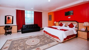 A hotel room with a large bed, a desk, a black sofa, and a red accent wall. - Mayfair Hotel (Dar es Salaam)
