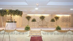 A stage with a white backdrop, floral arrangements, and a tiered cake on a table. - Mayfair Hotel (Dar es Salaam)