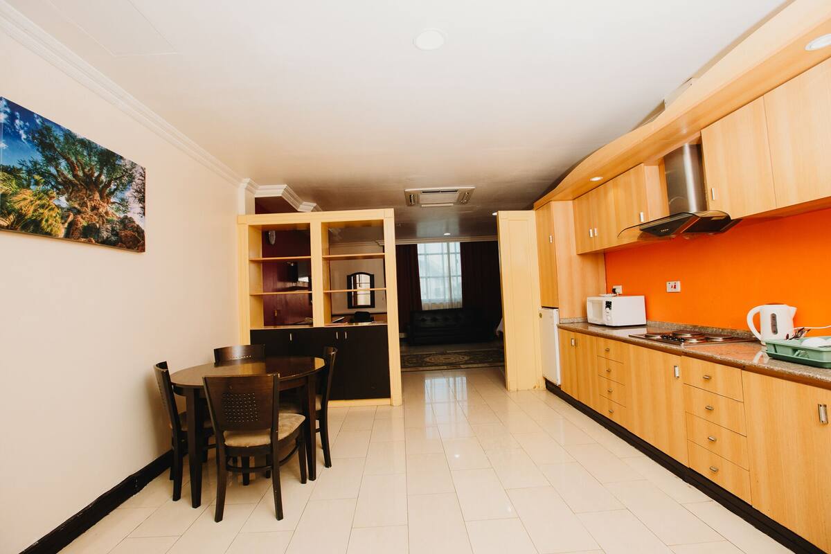 A modern kitchen with wooden cabinets, a dining table with chairs, and a painting on the wall.