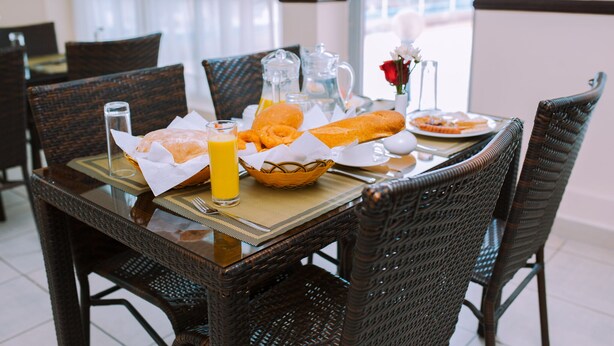 A dining table with a basket of bread, a glass of orange juice, and a pitcher of water. - Mayfair Hotel (Dar es Salaam)