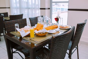 A dining table with a basket of bread, a glass of orange juice, and a pitcher of water. - Mayfair Hotel (Dar es Salaam)