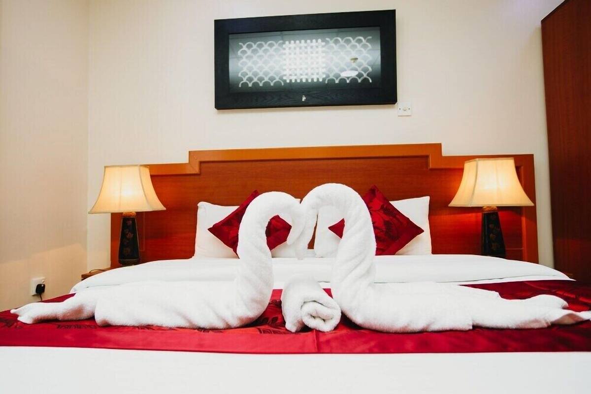 A hotel room with a bed, two bedside lamps, a framed picture on the wall, and a red bedspread.