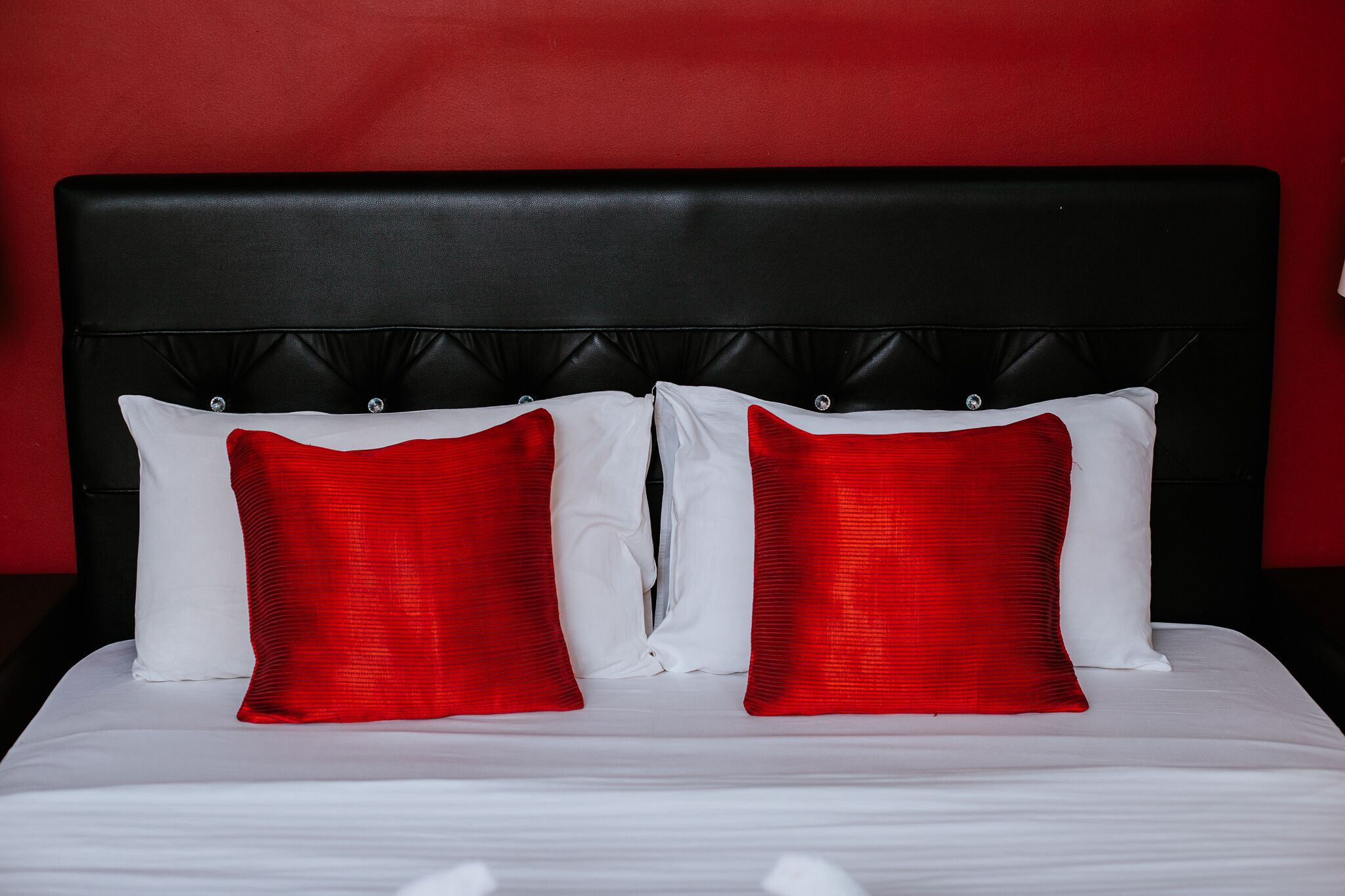 A bed with a black headboard and two red pillows.