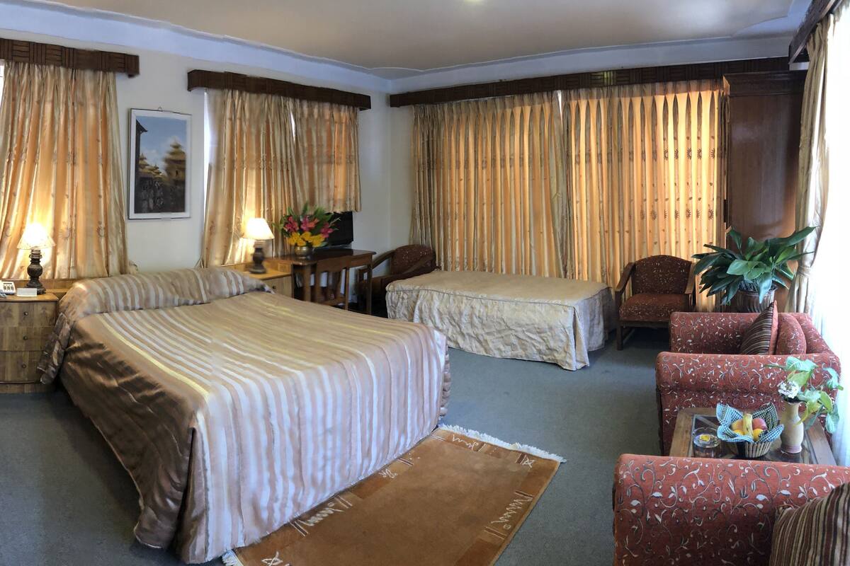 A hotel room with two beds, a desk, a chair, a sofa, and a large window with curtains.