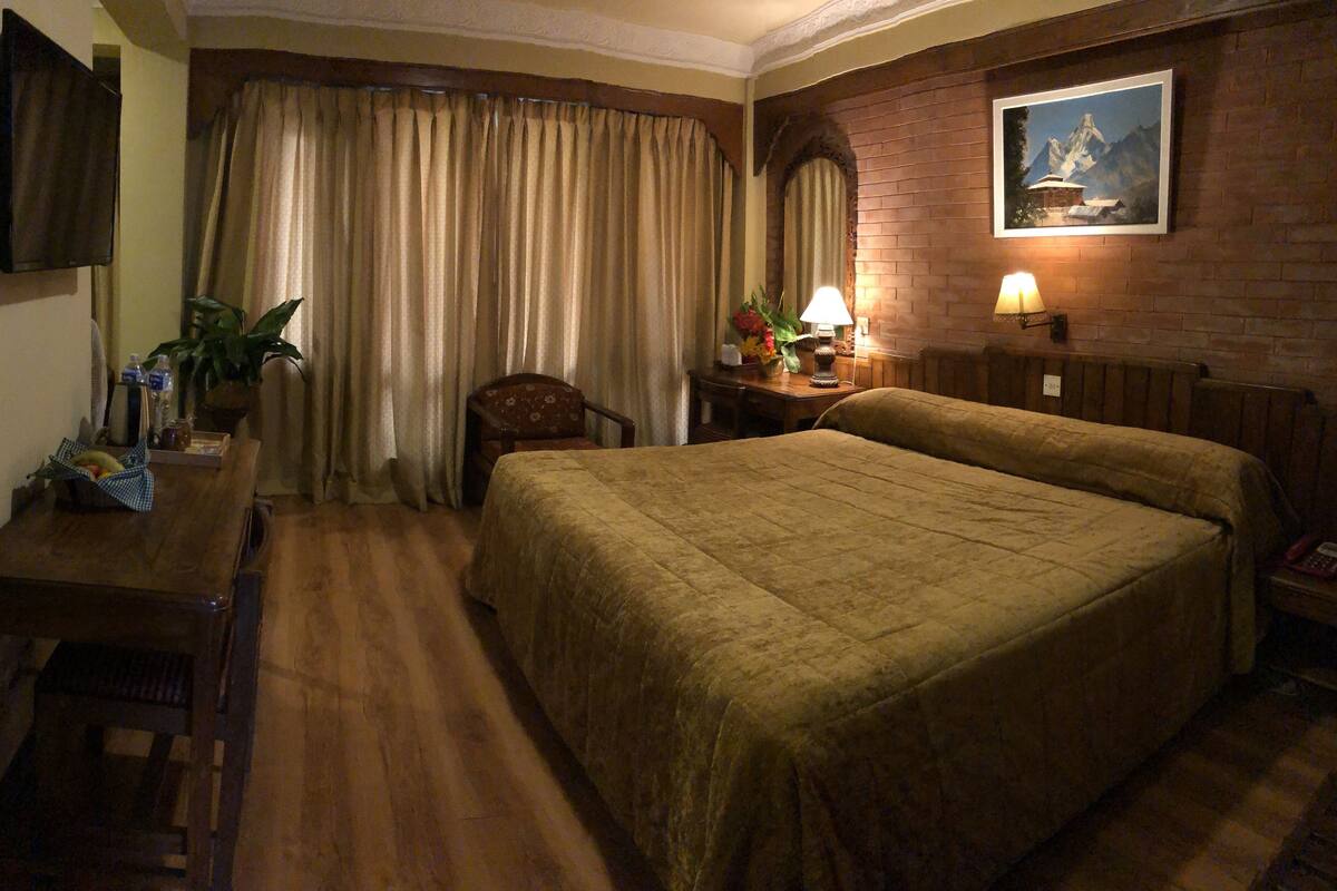 A hotel room with a large bed, a desk with a chair, a television, and a painting on the wall.