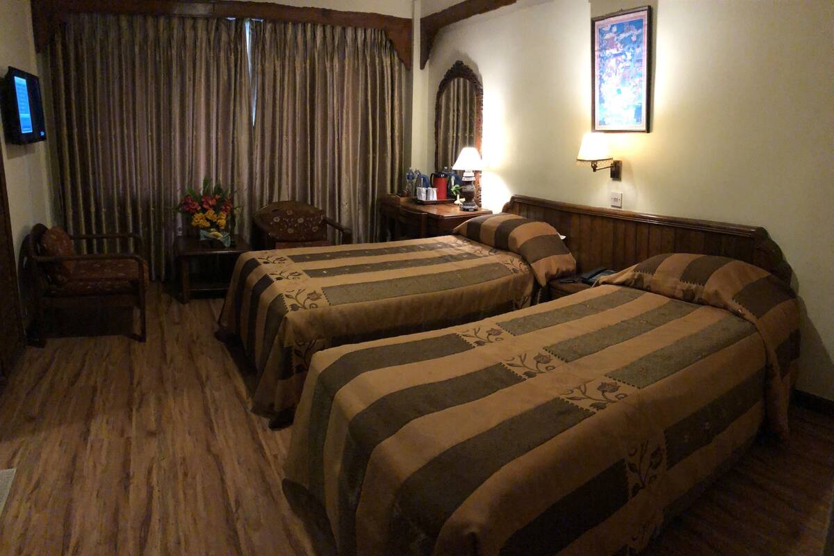 A hotel room with two beds, a desk with a lamp, a chair, and a television on the wall.