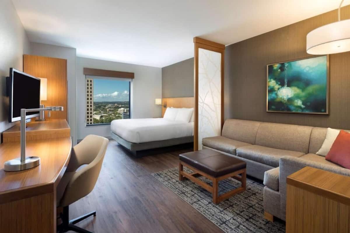 A hotel room with a bed, sofa, desk, TV, and a painting.
