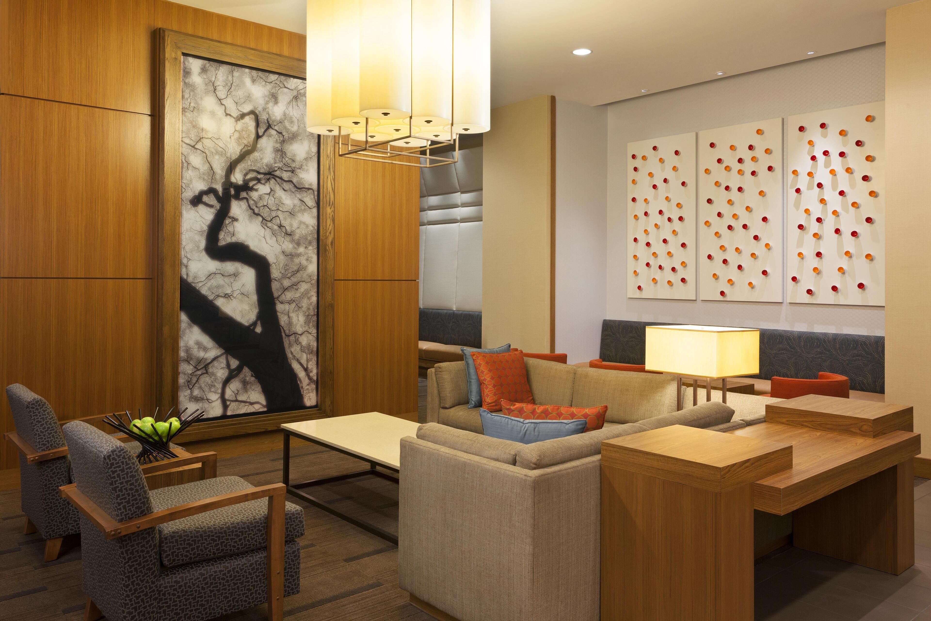 A modern hotel lobby with a seating area, a large abstract painting, and a wall with a pattern of red and orange spheres.