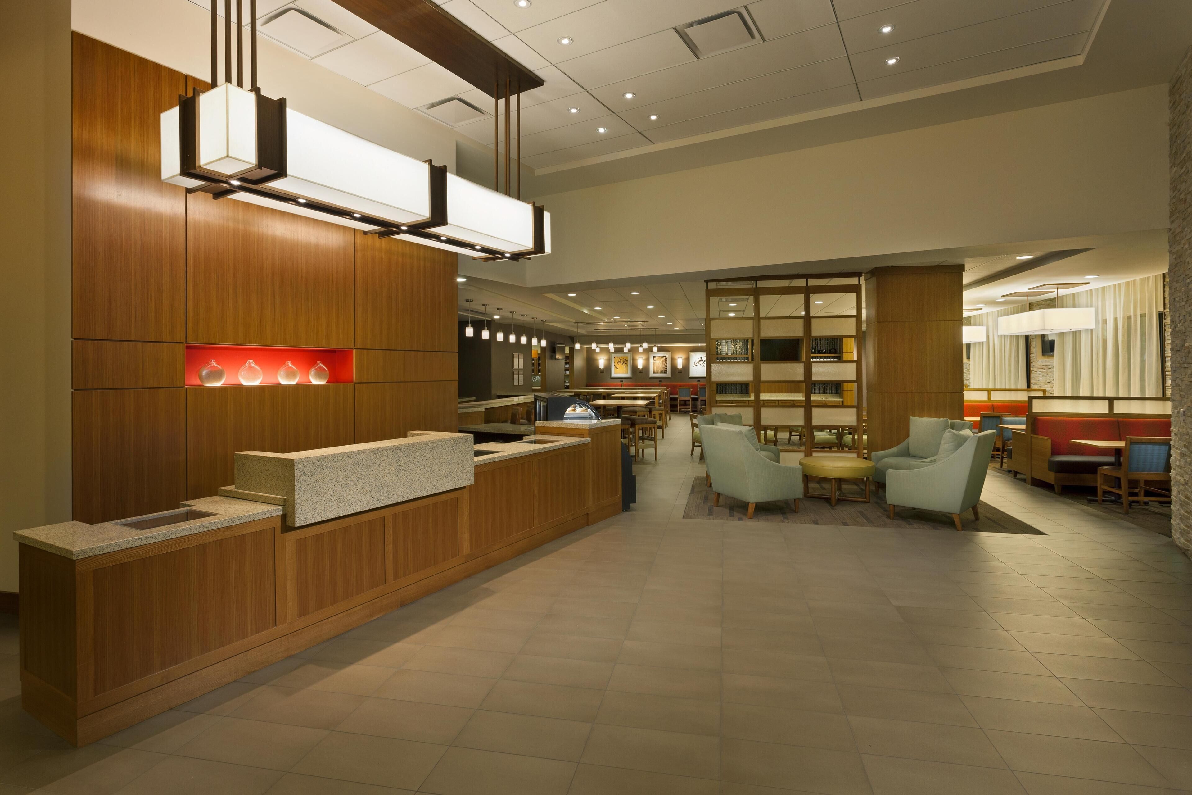 A modern hotel lobby with a reception desk, seating area, and a large window.