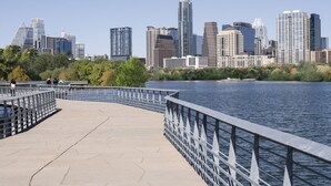 A waterfront promenade with a metal railing, a clear view of a city skyline with high-rise buildings, and a calm body of water. - Hyatt Place Austin Downtown (Austin)