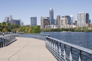 A waterfront promenade with a metal railing, a clear view of a city skyline with high-rise buildings, and a calm body of water. - Hyatt Place Austin Downtown (Austin)
