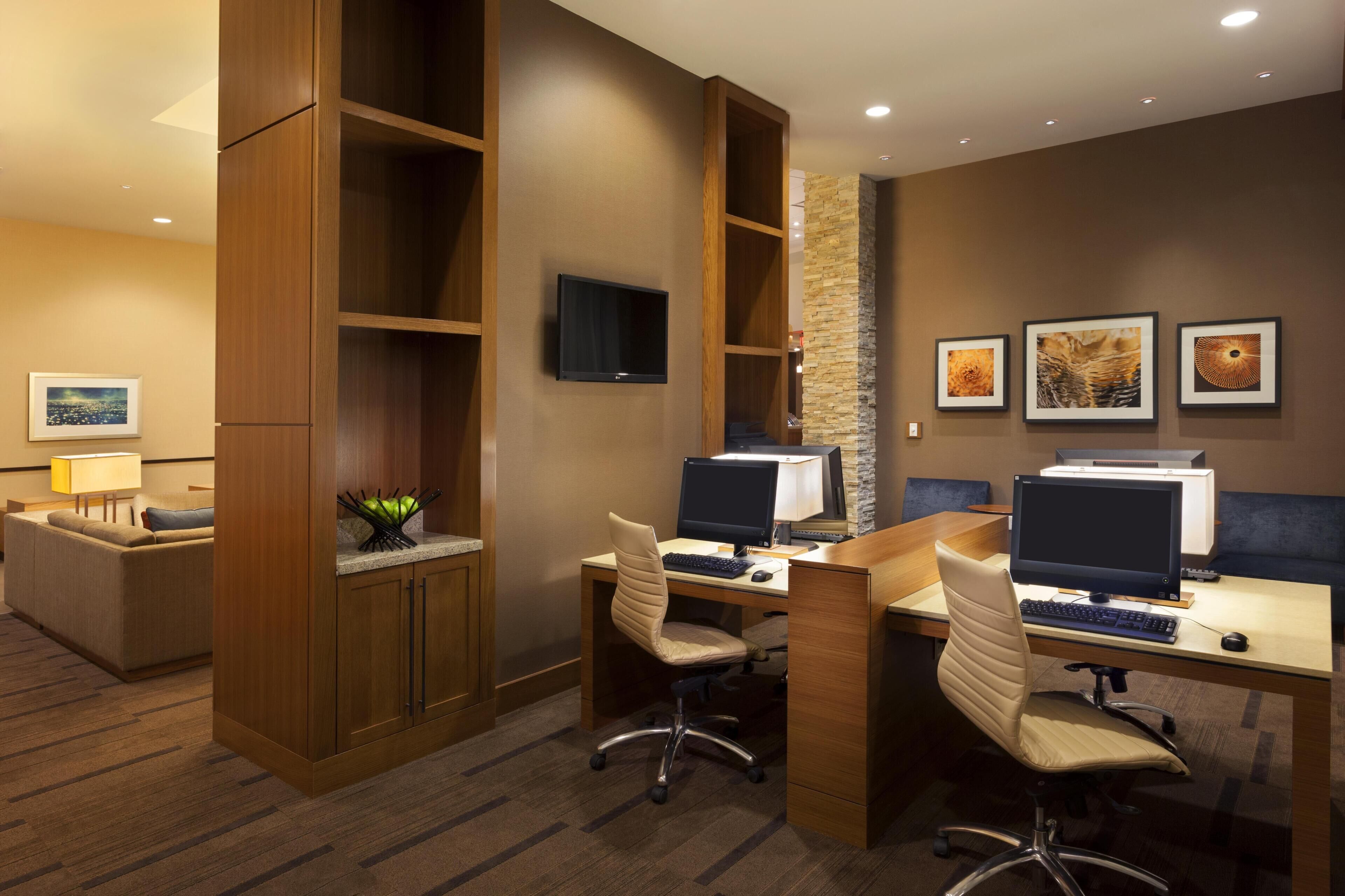A hotel room with a desk, two computers, a chair, a TV, and artwork on the wall.