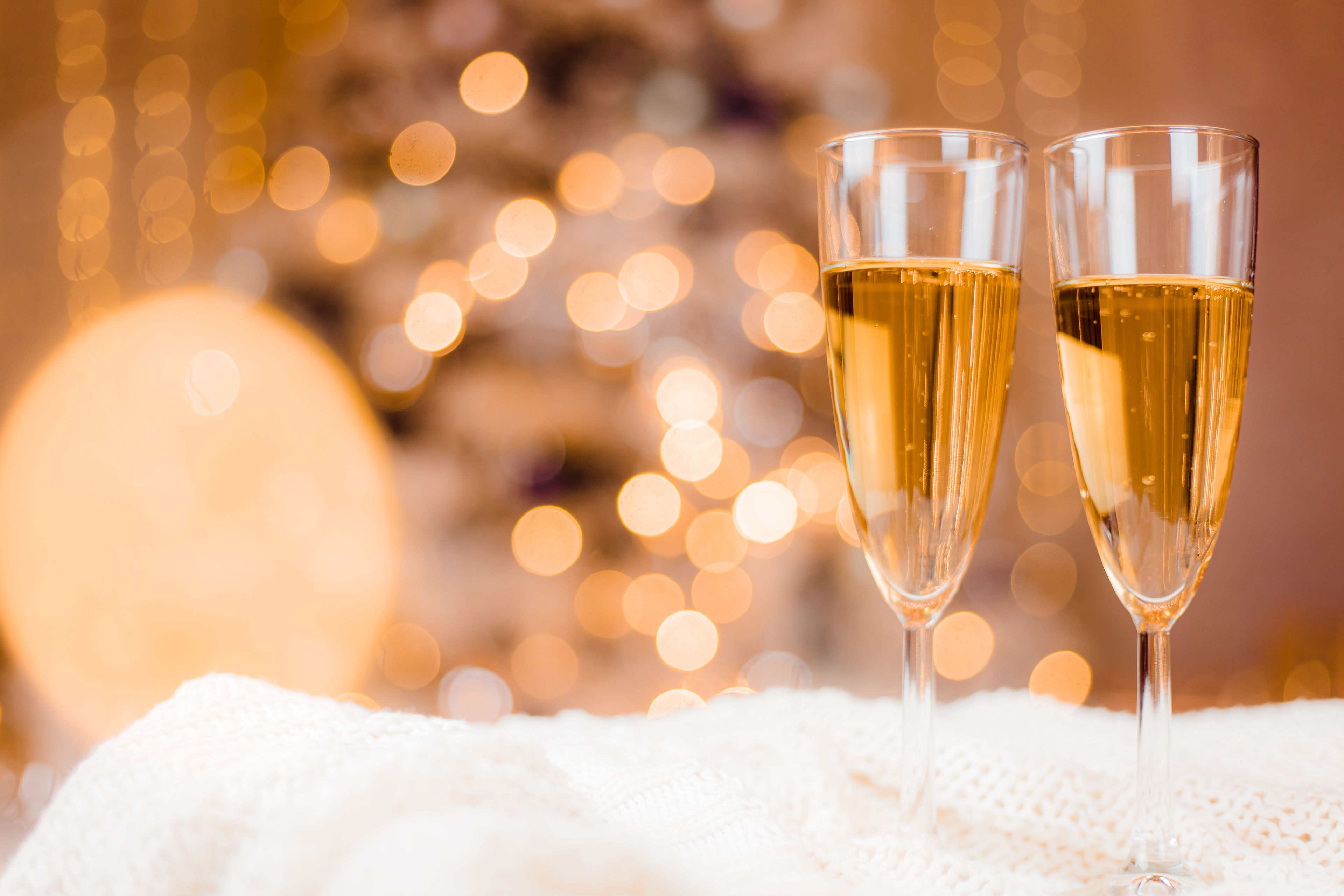 Två champagneglas på en vit, strukturerad yta, med en suddig bakgrund av ljus.