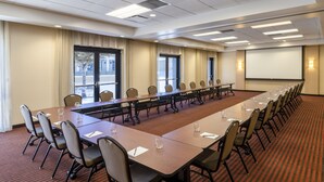 A conference room with a long table, chairs, a projector screen, and windows. - Hyatt Place Austin Downtown (Austin)