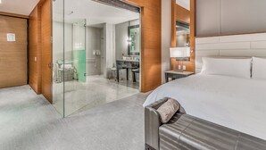 Een moderne hotelkamer met een groot bed, een douchecabine met glazen wanden, een bureau en een spiegel.
