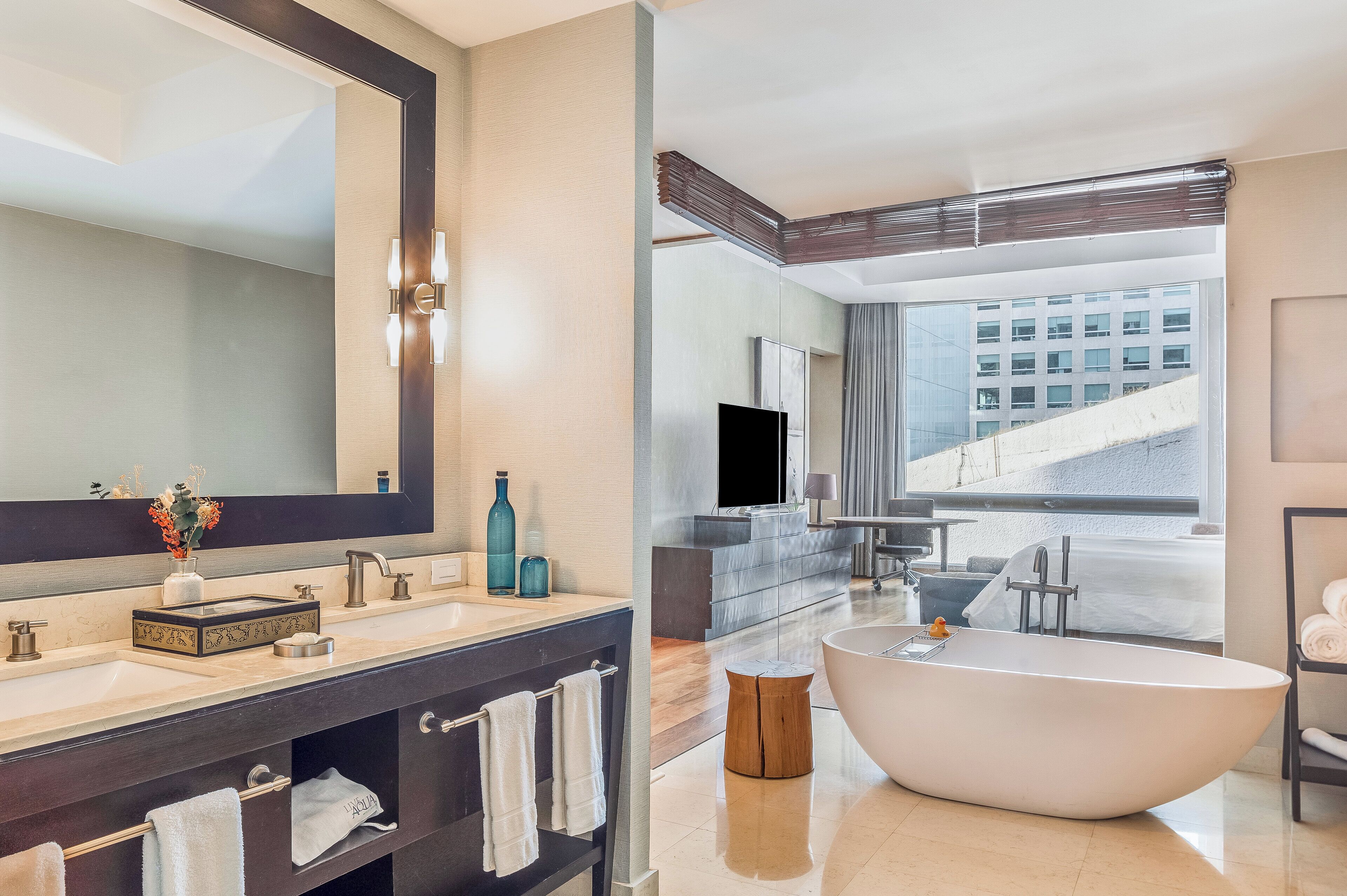 A modern bathroom with a large bathtub, a vanity with a mirror, and a view of a building through a large window.