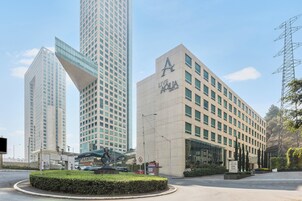 Un edificio moderno con un llamativo logotipo 'A' y señalización 'Live Aqua', rodeado de otros edificios altos y un área ajardinada con un camino de acceso circular.