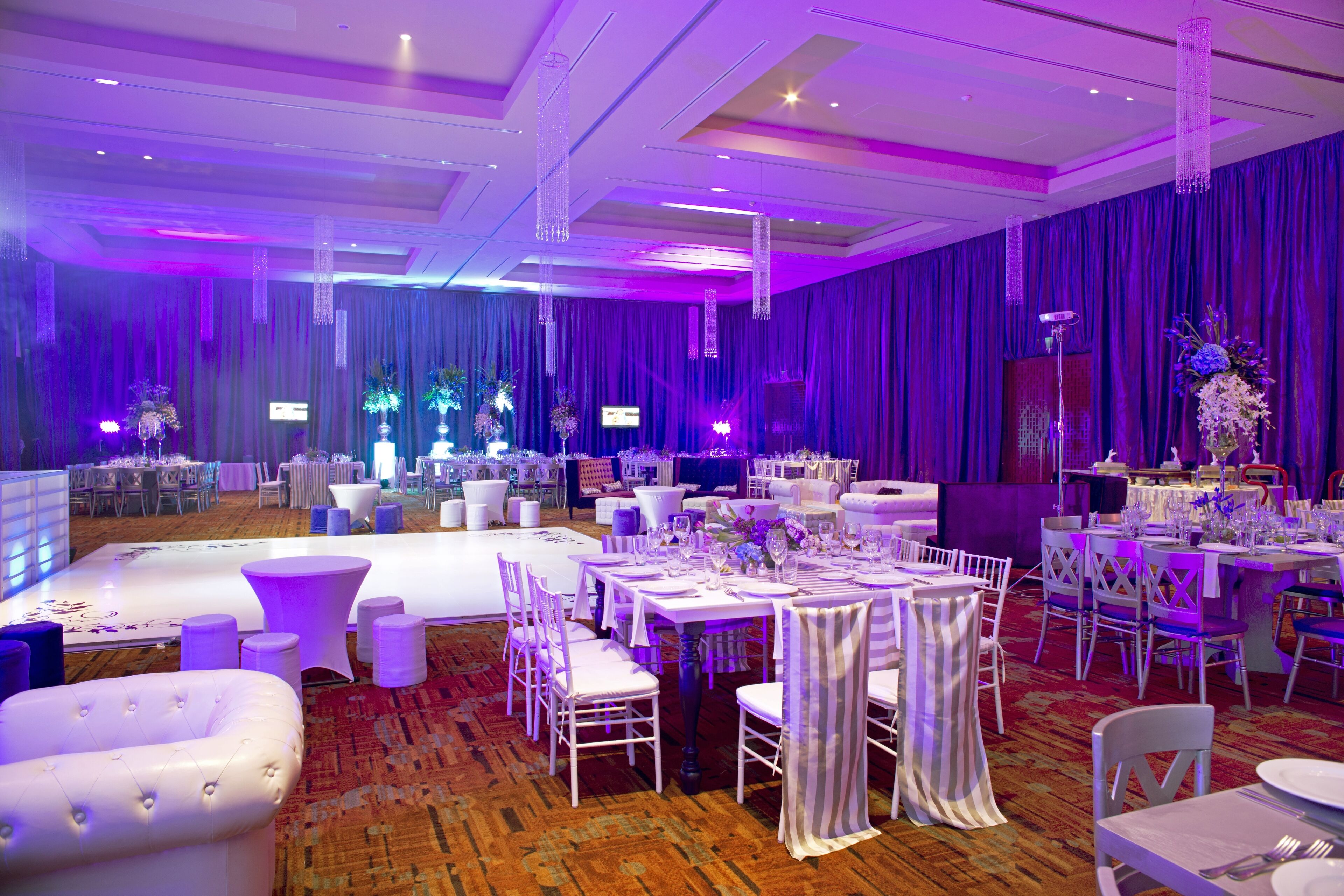 Une salle de banquet avec des tables rondes, des chaises blanches et des rideaux violets.