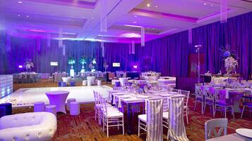 Une salle de banquet avec des tables rondes, des chaises blanches et des rideaux violets.