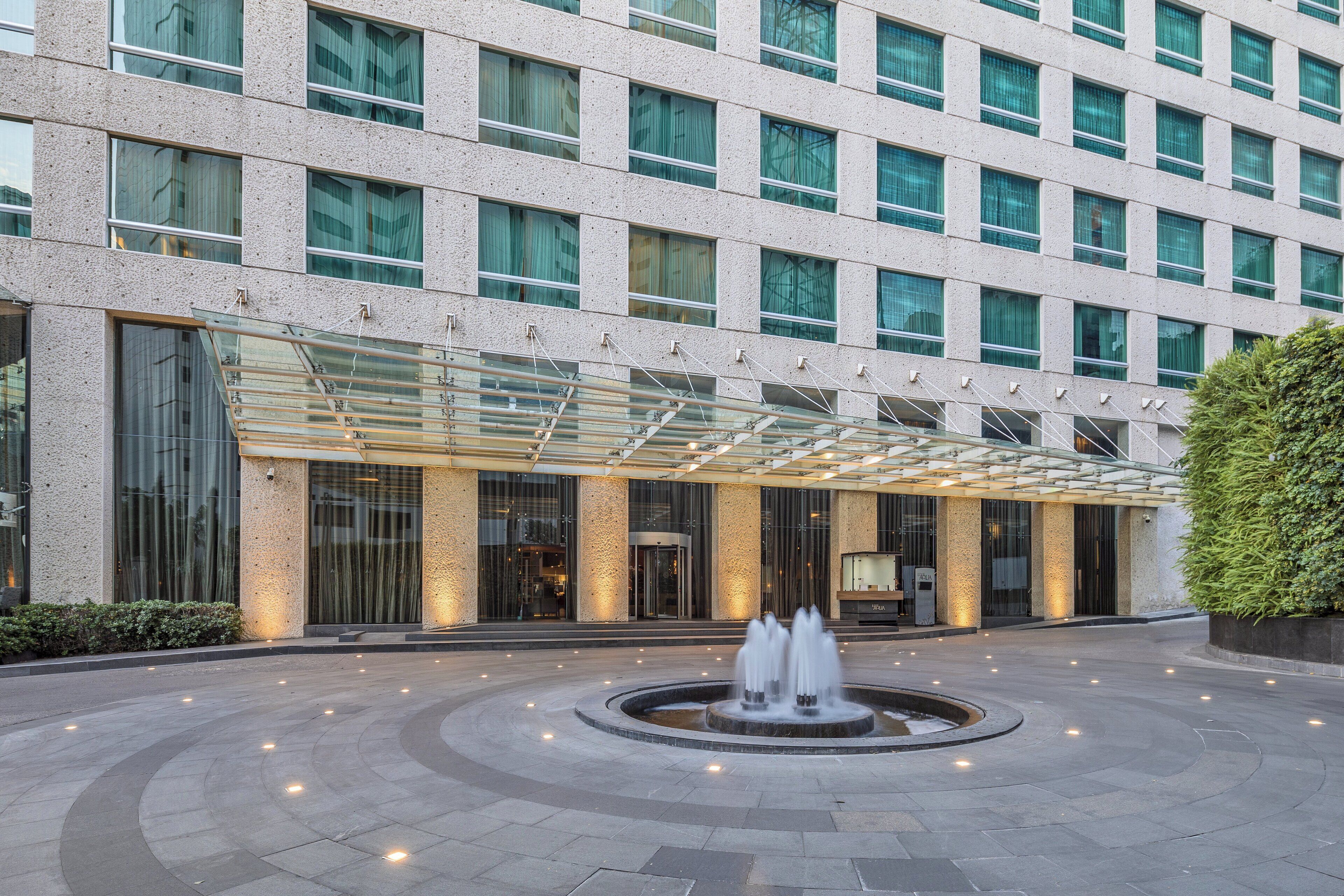A modern hotel with a central courtyard featuring a fountain, large windows, and a covered walkway.