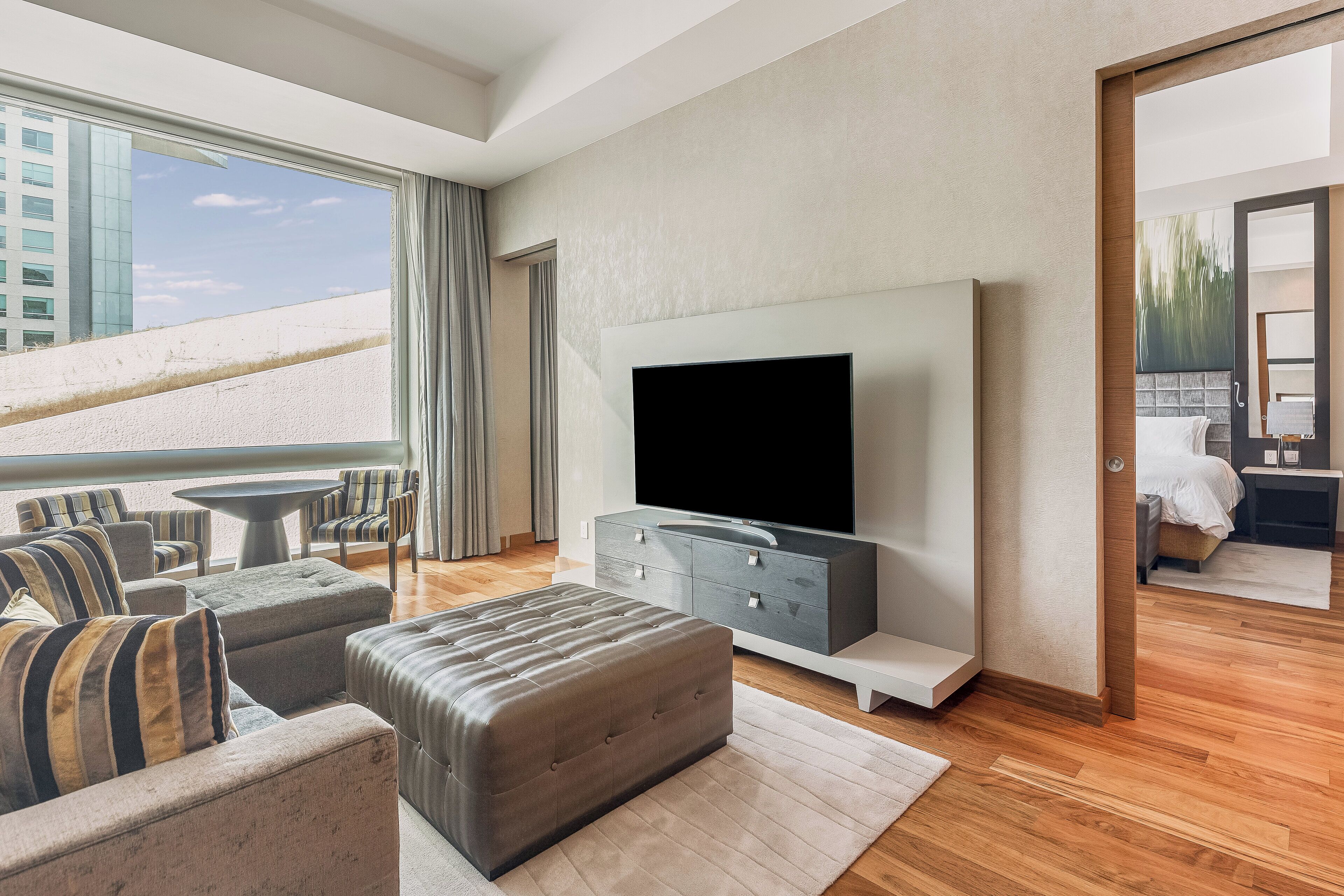 Uma sala de estar moderna com uma televisão de tela plana grande, assentos confortáveis e vista para a paisagem urbana.