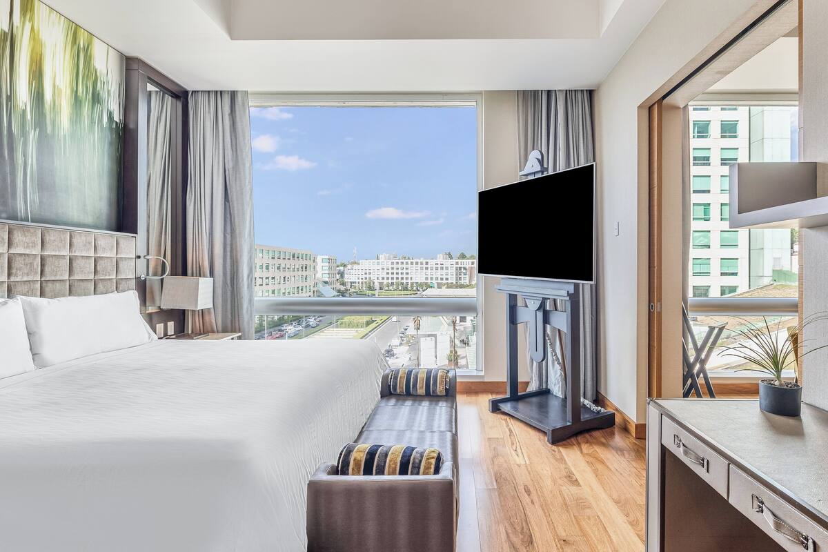 Habitación de hotel moderna con una cama grande, televisión, escritorio y vistas de la ciudad.
