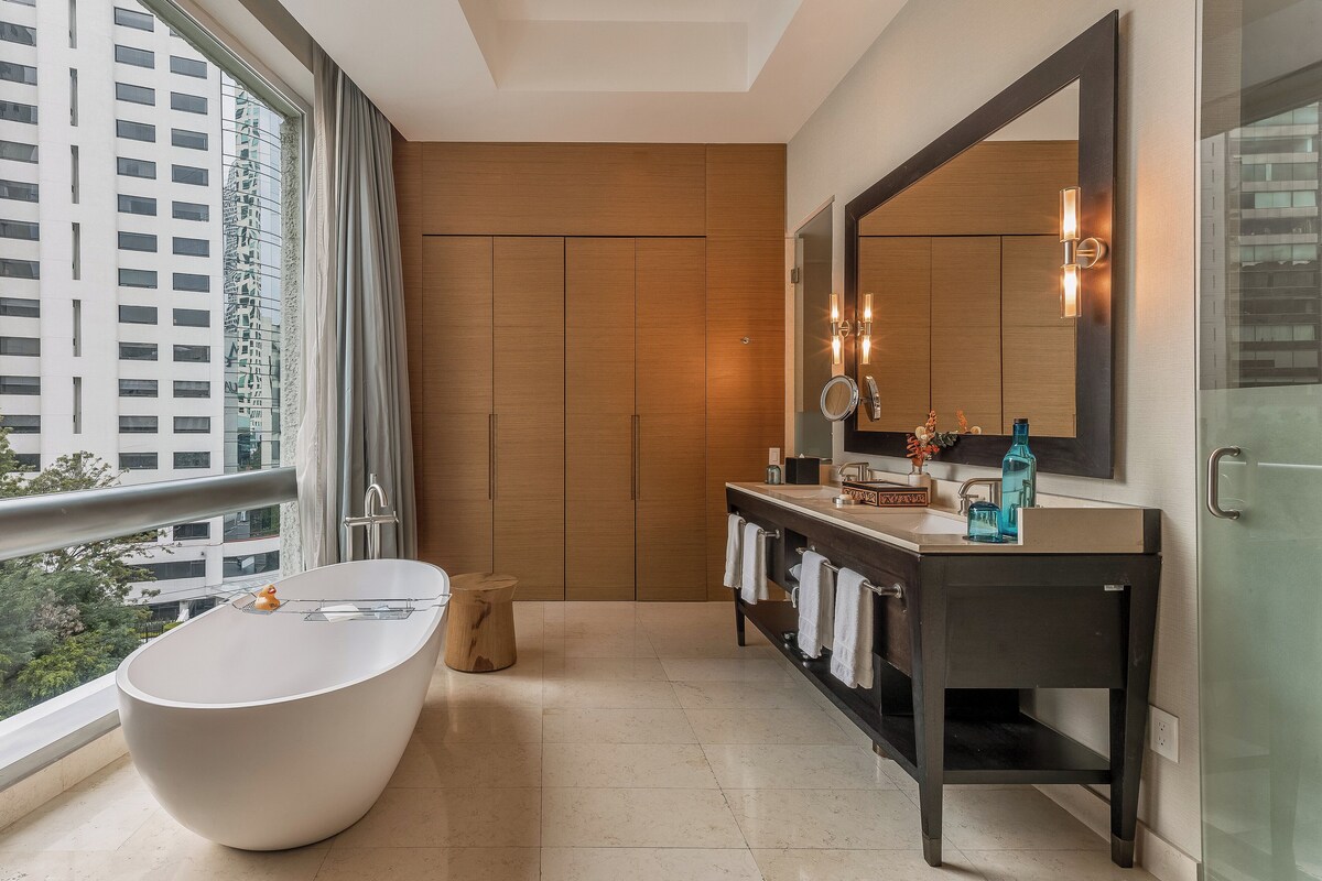 Een moderne badkamer met een vrijstaand bad, een donkere wastafelmeubel en een grote spiegel.