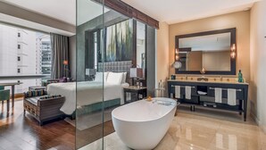 Een moderne hotelkamer met een groot bed, een badkamer met glazen wanden, een badkuip, een wastafel met spiegel en uitzicht op de stad door grote ramen.