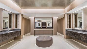 Relax in a serene bathroom with a round ottoman, two large mirrors, and a granite-like countertop.