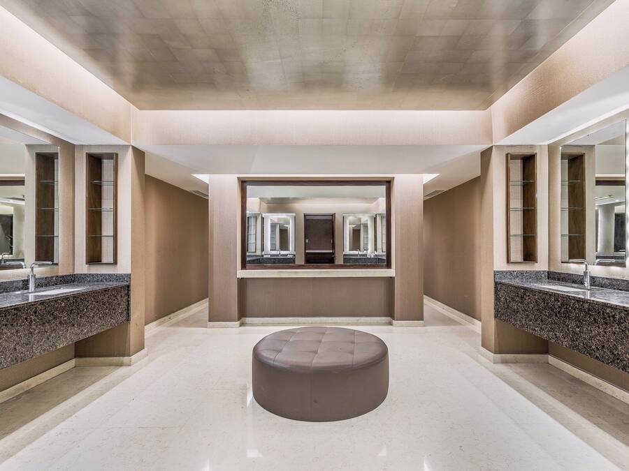 Un baño moderno con un banco redondo central, espejos grandes y encimeras de granito.