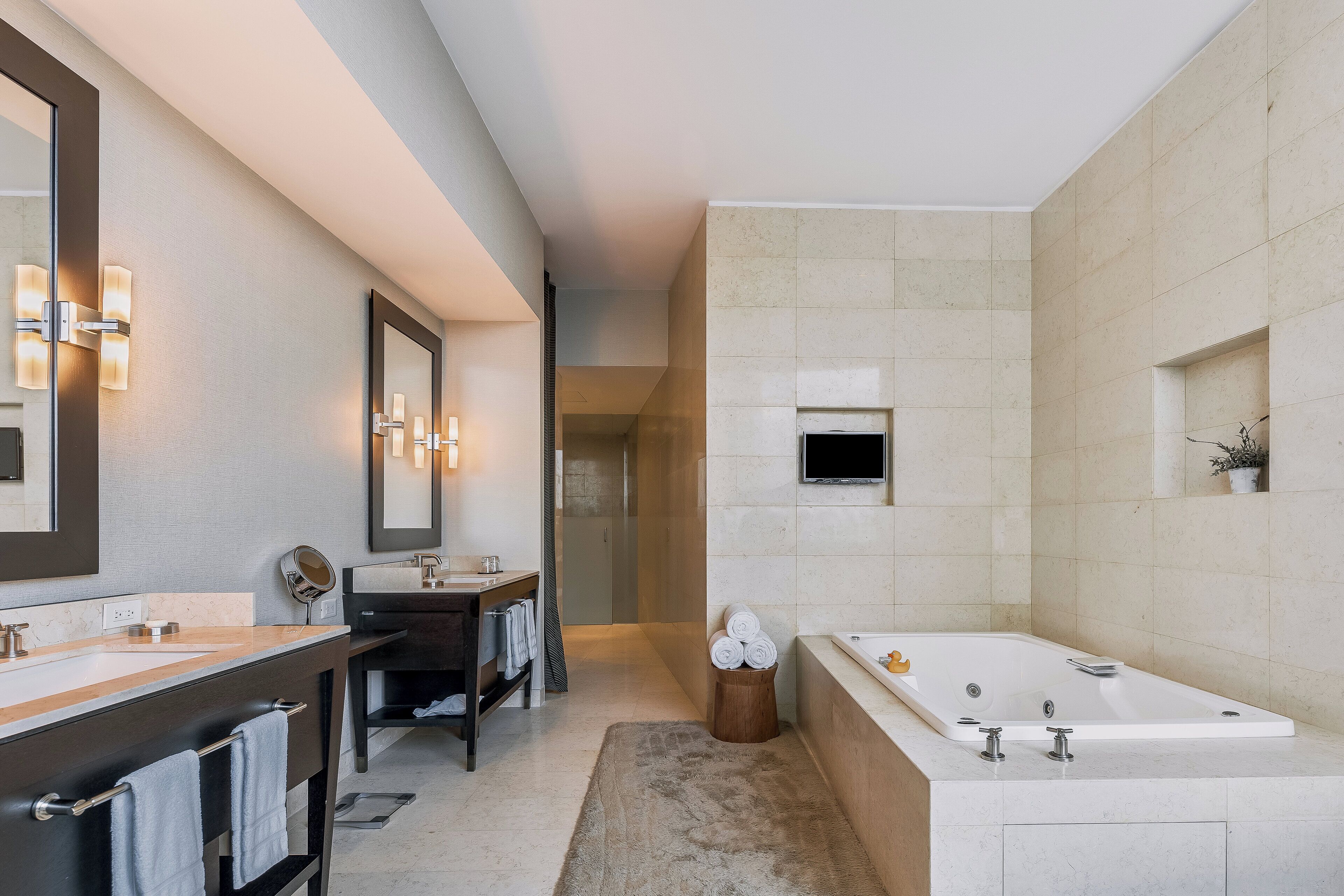 A modern bathroom with a large mirror, two sinks, a bathtub, and a shower area.