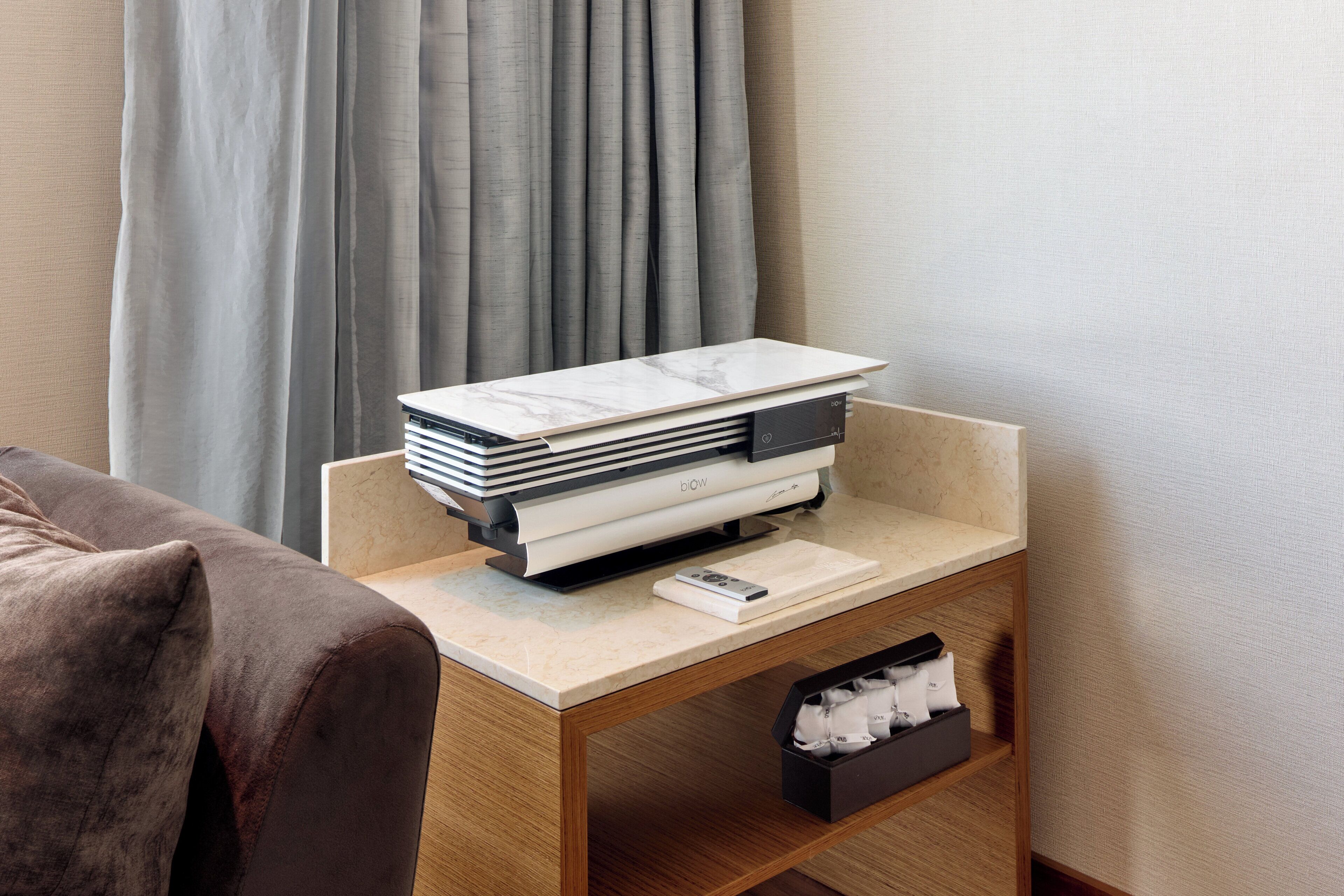 A hotel room with a wooden nightstand holding a printer, a remote control, and a tissue box.