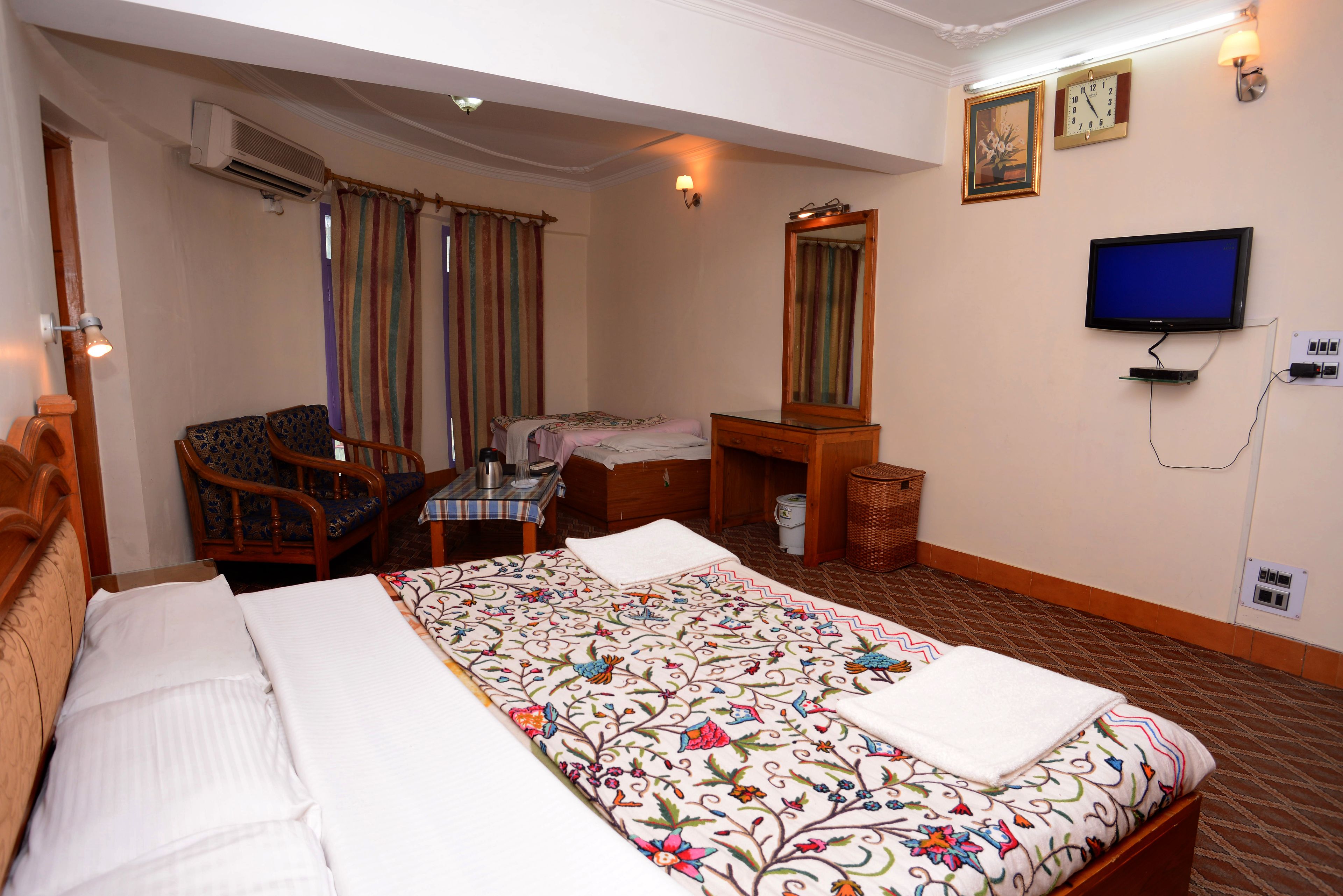 A hotel room with a bed, a desk, a chair, a television, and an air conditioning unit.