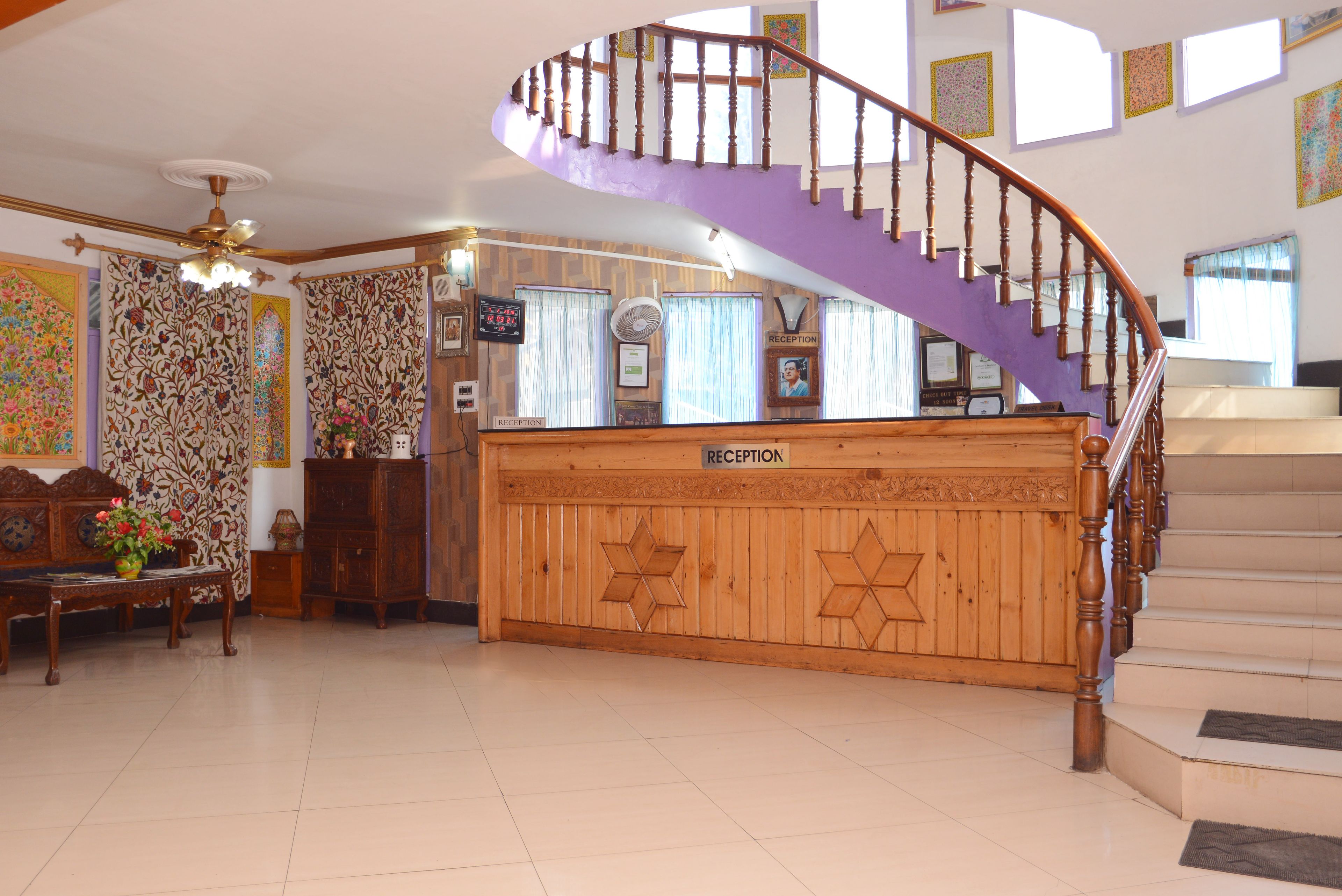 Zona de recepción con mostrador de madera, escalera morada y ventilador de techo.